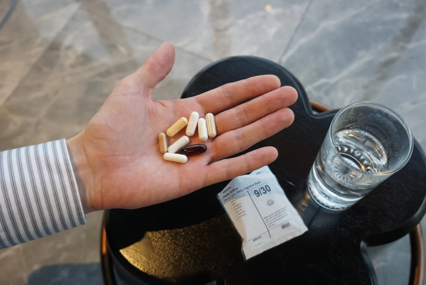 The eight capsules of one 30BASE sachet held in a palm beside a glass of water.