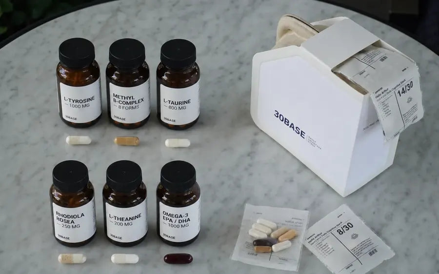 Separate bottles of L-Tyrosine, Methyl B-Complex, L-Taurine, Rhodiola Rosea, L-Theanine and Omega-3 with their capsules, beside the 30BASE box and one daily packet holding the same capsules.