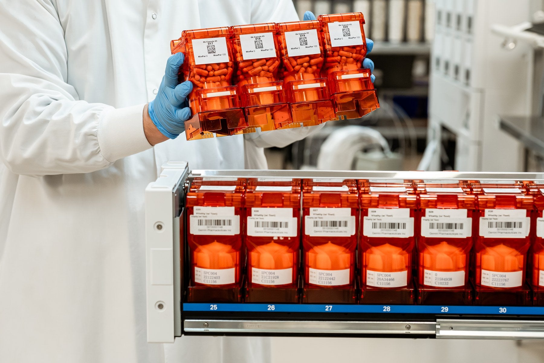 Operator in lab coat and blue gloves handling barcoded compound modules at the production facility