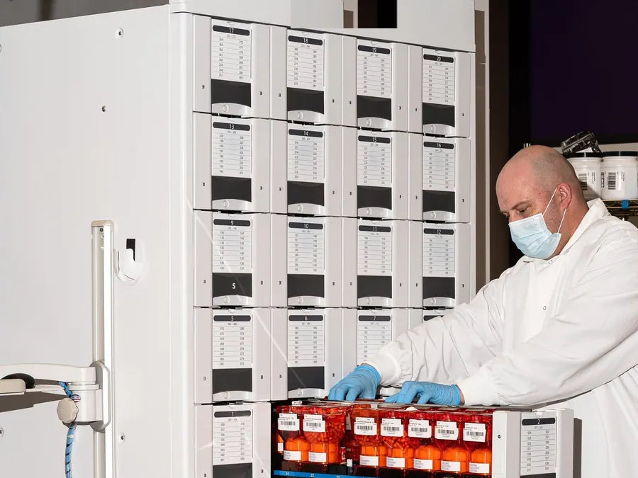 A masked operator loading a tray of barcoded compound modules into the line.