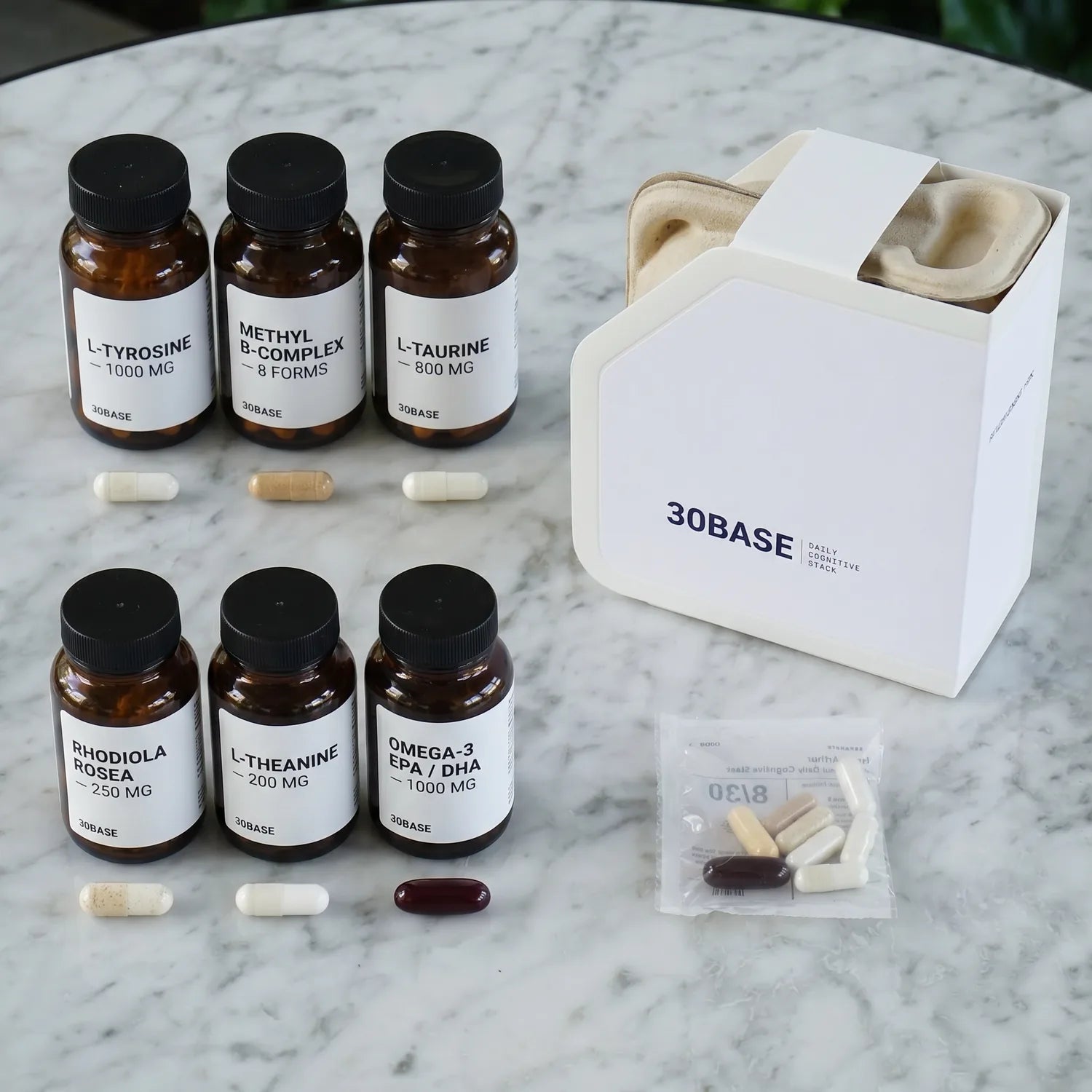 Separate jars of L-Tyrosine, Methyl B-Complex, L-Taurine, Rhodiola Rosea, L-Theanine and Omega-3 with their capsules, beside the 30BASE box and one daily sachet holding the same capsules.