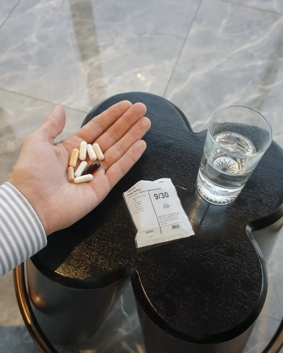 The eight capsules of a 30BASE daily sachet held in an open palm beside a glass of water