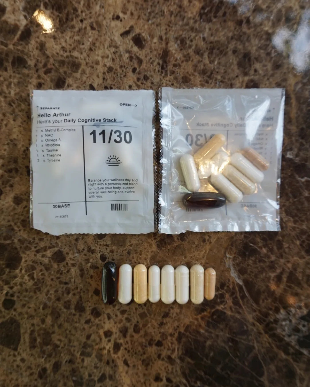 The eight capsules of one 30BASE daily sachet laid out in a row on marble, next to the sealed sachet that holds them