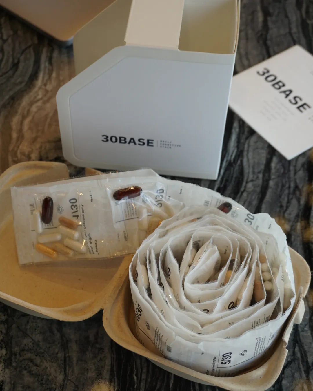 An open 30BASE box with a daily sachet and its capsules, including the dark fish-oil softgel