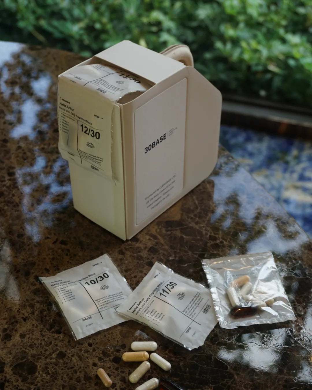 A 30BASE box on marble with an opened daily sachet and its capsules beside it