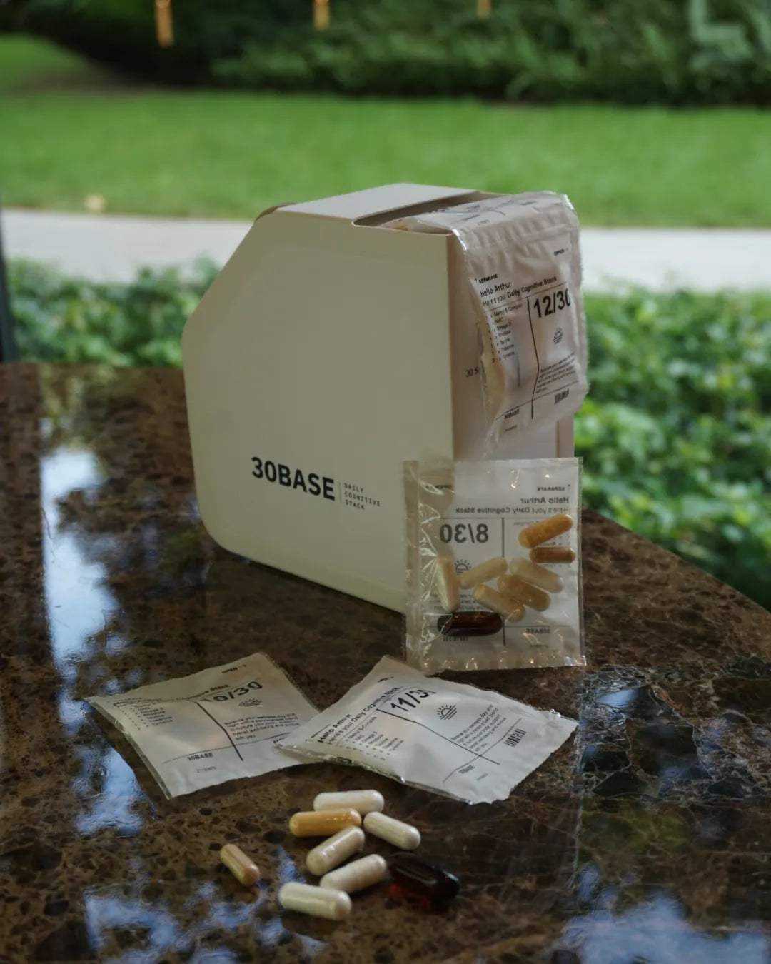 The 30BASE Daily Cognitive Stack box on a marble table outdoors, a daily sachet dispensing with capsules in front.
